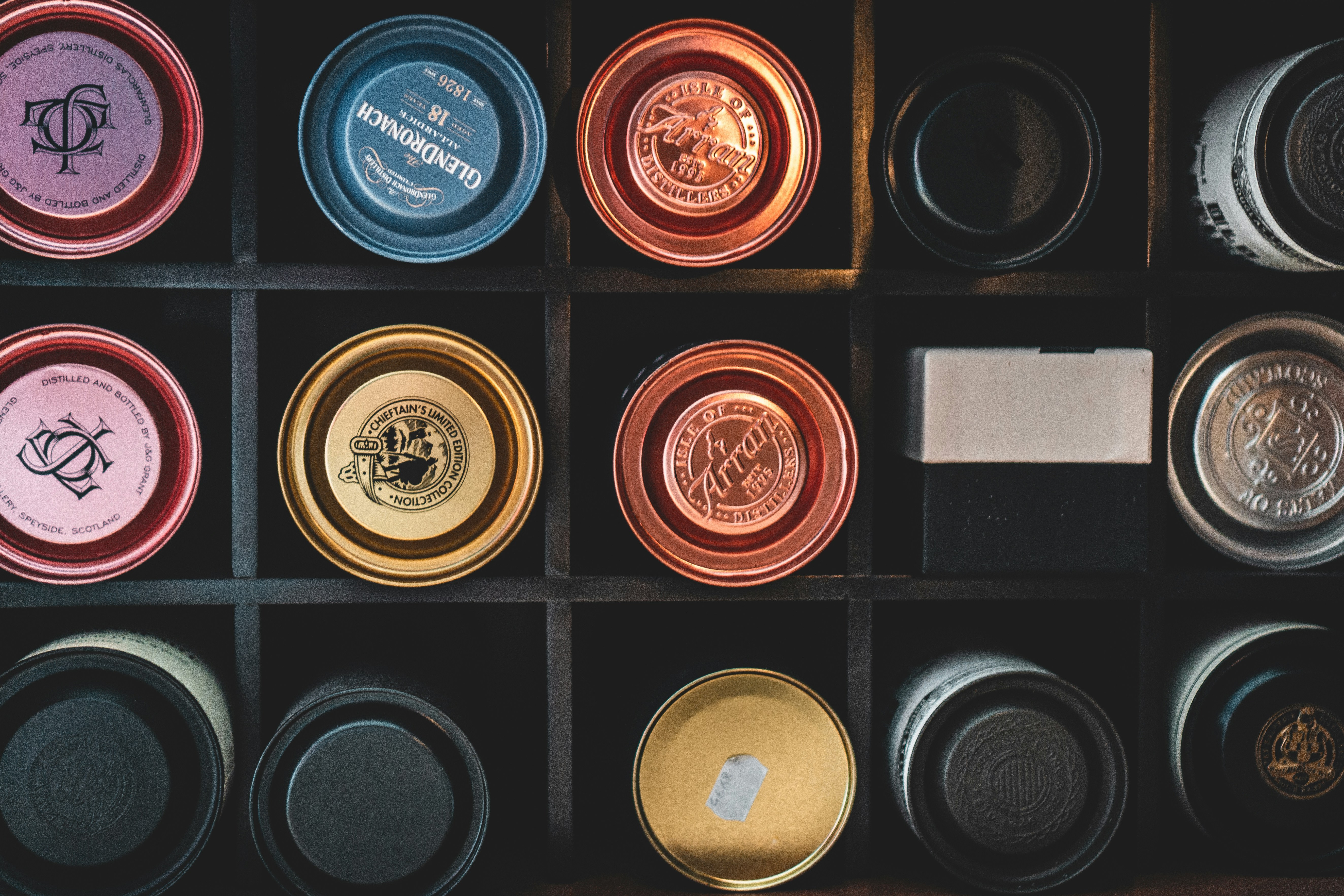 An image of a dark wooden whisky rack filled with vertically lined up whisky boxes ranging from wine red, gold, orange to silver and black.